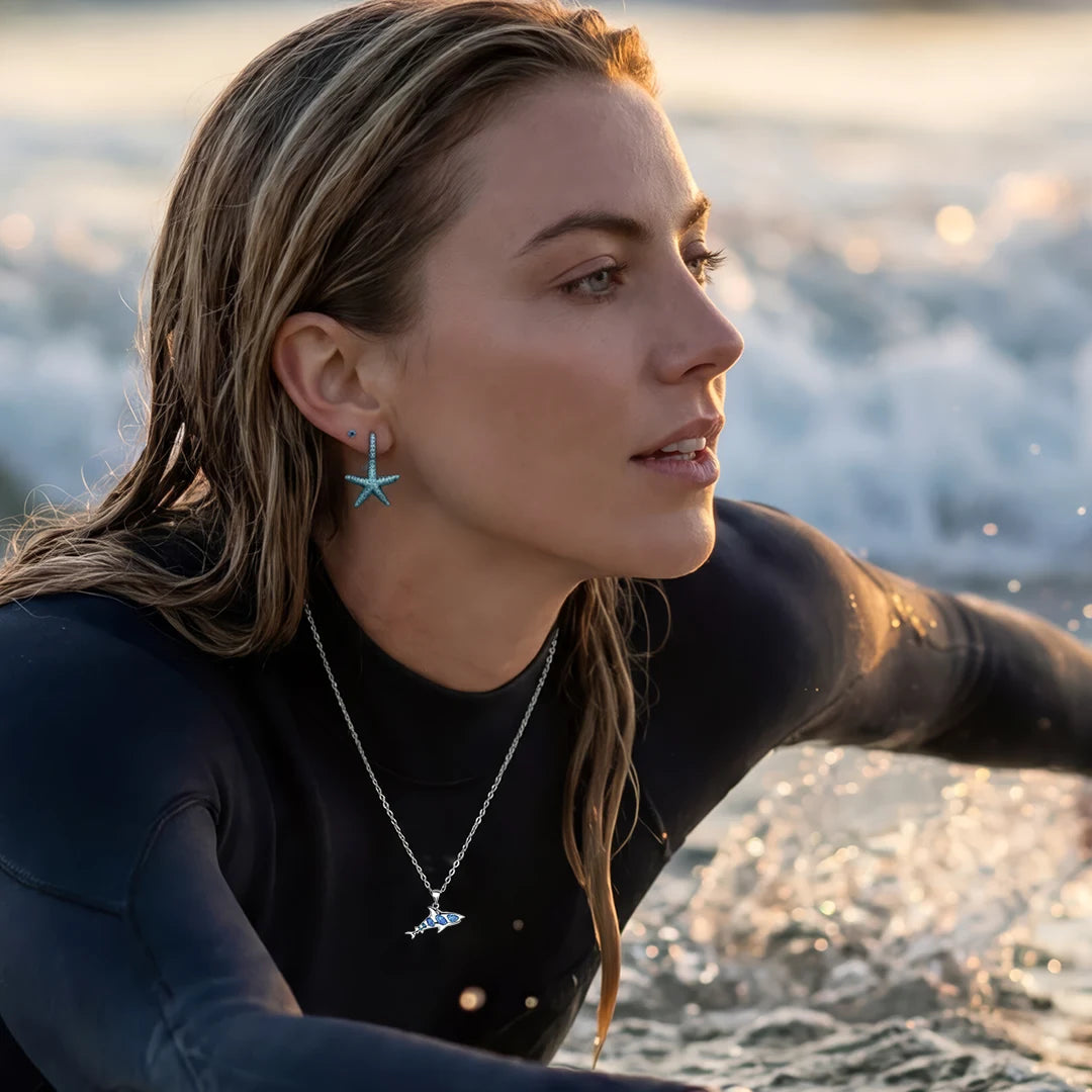 Surfer wearing starfish earrings and shark necklace at sunset